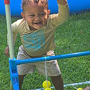 Marcus is registered to the contest to win money with this photo: toddler, child, smiling, outdoor, grass, barefoot, toy, plastic, play, game, yellow, ball, green, happy, person, clothing, shorts, long_sleeve, curly_hair, summer