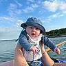 baby, child, person, water, lake, blue_sky, clouds, hat, clothing, tattoo, arm, hand, outdoor, nature, summer, sunlight, expression, holding, trees, water_sports