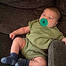 baby, infant, pacifier, green_clothing, knitwear, blue_socks, striped_socks, couch, furniture, relaxed, indoor, child, cute, young, person, seated, expression, skin, footwear, comfort