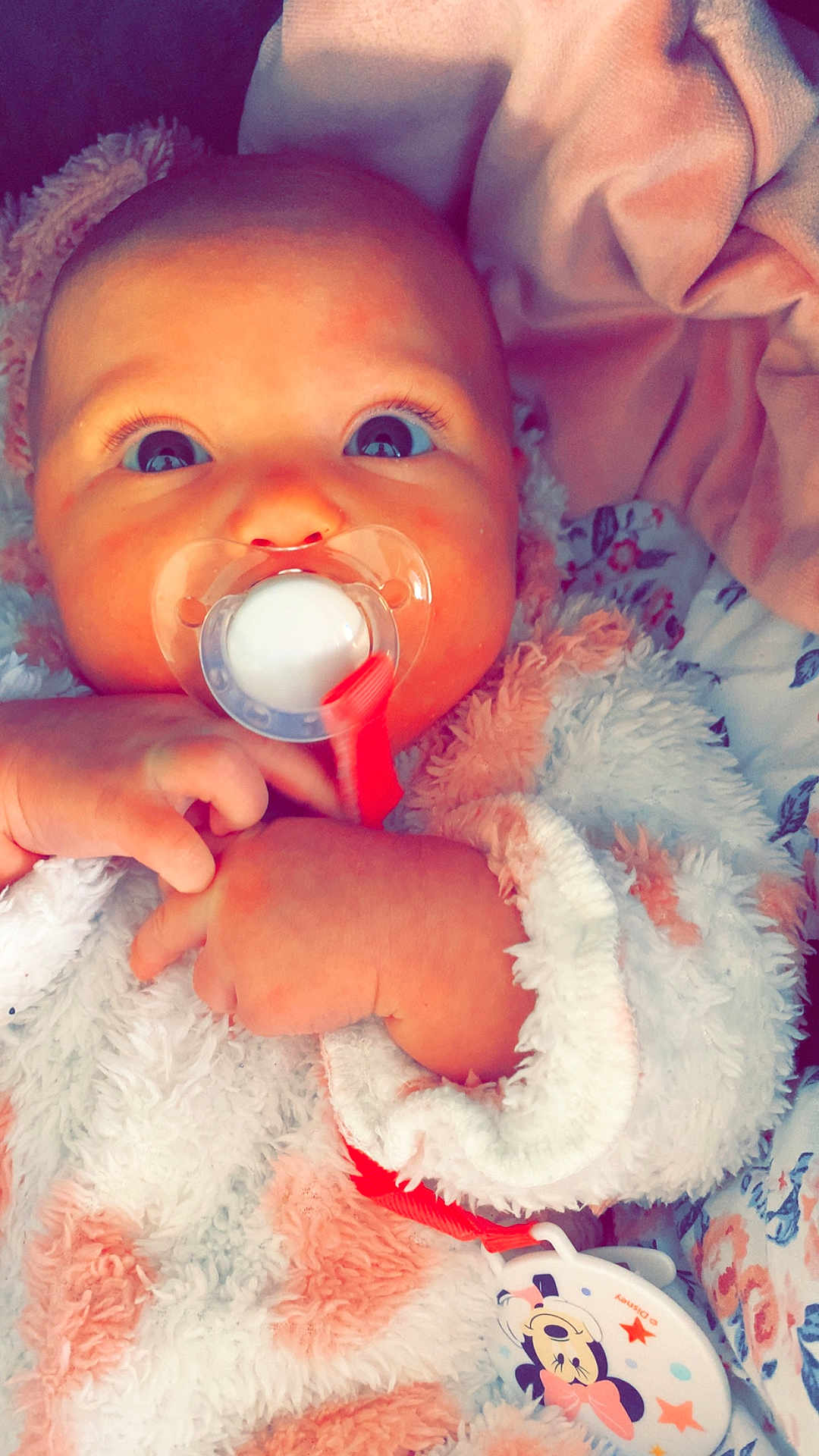 Aïlys a rejoint le concours — aidez-le/la à gagner de superbes lots ! baby, pacifier, blanket, infant, hands, face, wide_eyes, soft_texture, floral_pattern, clothing, cute, child, sleepwear, comfort, indoors, portrait, newborn, resting, small_hands, closeup