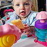 baby, child, toy, indoor, playtime, snack, colorful, curious, face, expression, blue_eyes, clothing, plastic, table, seat, person, infant, young, hand, closeup