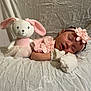 baby, sleeping, infant, plush_toy, bunny, pink_clothing, headband, mittens, fabric, textured_background, soft_lighting, cute, peaceful, child, portrait, indoors, resting, toy, decorative_flower, blanket