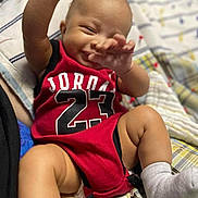 Amarie is registered to the contest to win money with this photo: baby, child, infant, smiling, red_clothing, jordan, number_23, sock, blanket, quilt, happy, lying_down, hand_up, cute, skin, person, indoors, playful, young, apparel