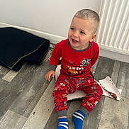 Matas Gluskovas joined the competition — help win amazing prizes! toddler, child, pajamas, red_clothing, sitting, floor, wooden_floor, smiling, blue_socks, indoors, radiator, paper, mat, playful, happy, cute, person, young_child, casual, home