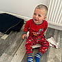 toddler, child, pajamas, red_clothing, sitting, floor, wooden_floor, smiling, blue_socks, indoors, radiator, paper, mat, playful, happy, cute, person, young_child, casual, home
