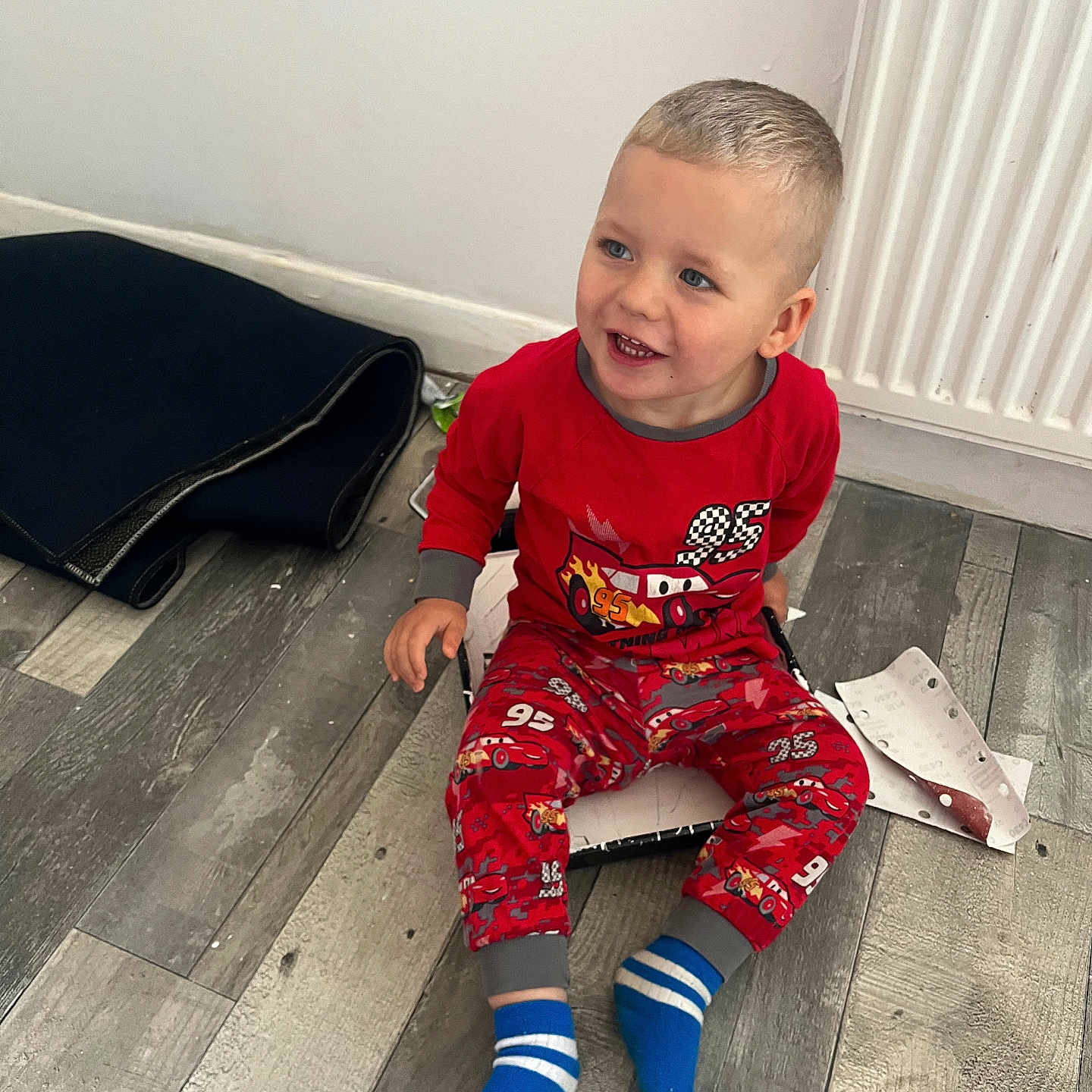 Matas Gluskovas joined the competition — help win amazing prizes! blue_socks, casual, child, cute, floor, happy, home, indoors, mat, pajamas, paper, person, playful, radiator, red_clothing, sitting, smiling, toddler, wooden_floor, young_child