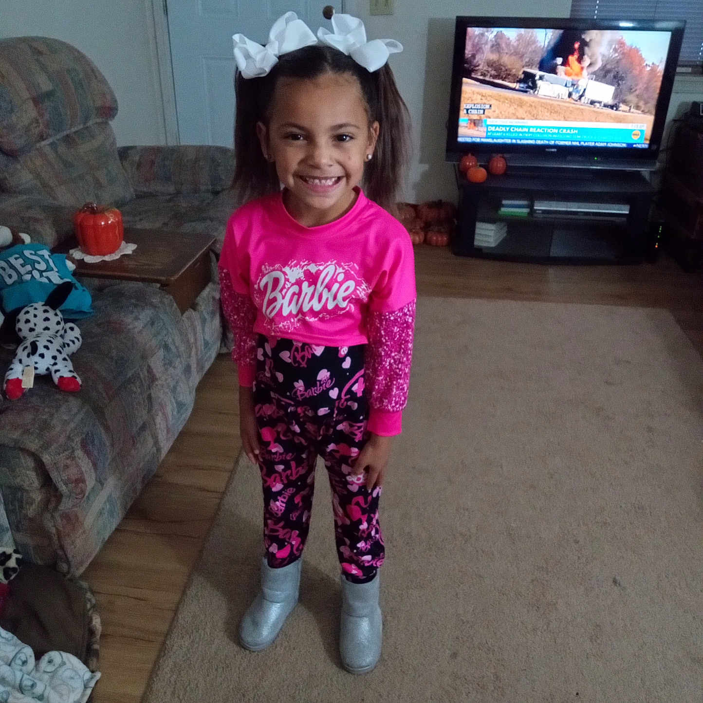 Ma'Kiah is registered to the contest to win money with this photo: boots, carpet, child, couch, decor, door, furniture, girl, hair_bows, happy, indoors, living_room, news_broadcast, pink_clothing, pumpkins, smiling, standing, television, toy, wooden_floor