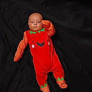 Oakley is registered to the contest to win money with this photo: baby, infant, onesie, orange_clothing, pumpkin_costume, lying_down, black_background, cute, child, portrait, one_person, indoors, looking_at_camera, baby_clothes, baby_feet, baby_face, baby_hand, soft_fabric, costume, seasonal