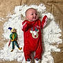 Oakley is registered to the contest to win money with this photo: baby, infant, red_onesie, reindeer, holiday, christmas, toy, elf, figurine, blanket, powder, smiling, cute, lying_down, feet, face, child, indoor, festive, playful
