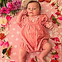 baby, infant, pink_clothing, flower_arrangement, blanket, polka_dot, lying_down, skin, face, head, legs, hands, berries, petals, nature, soft_texture, cute, portrait, outdoor_style, peaceful