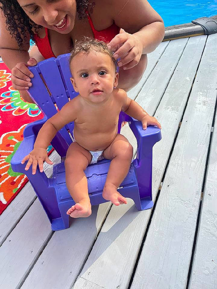 Kyla is registered to the contest to win money with this photo: baby, baby_toddler_clothing, barefoot, blue, event, face, foot, fun, happy, human_leg, joy, leisure, outdoor_furniture, people_on_beach, person, recreation, smile, summer, thigh, toddler