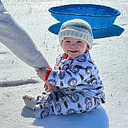 John joined the competition — help win amazing prizes! baby, child, snow, winter, outdoor, cold, knit_hat, onesie, smile, blue_pool, sunlight, holding_hand, sitting, grass, shadow, warm_clothing, happy, person, playing, daytime