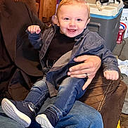 John is registered to the contest to win money with this photo: adult_hand, casual_clothing, cat, child, cooler, cozy, cute, dark_shirt, furniture, happy, home, indoor, jeans, person, playful, portrait, seated, smiling, toddler, young_child