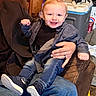 adult_hand, casual_clothing, cat, child, cooler, cozy, cute, dark_shirt, furniture, happy, home, indoor, jeans, person, playful, portrait, seated, smiling, toddler, young_child