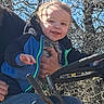 John is registered to the contest to win money with this photo: baby, blue_jacket, casual, child, clothing, daytime, face, hand, happy, holding, nature, outdoor, person, portrait, sky, smiling, sunlight, toddler, trees, vehicle