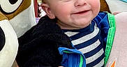 John joined the competition — help win amazing prizes! adult_hand, blue_jacket, cartoon_character, casual_clothing, child, cute, face, folded_clothes, happy, holding, indoor, mascot, person, playful, portrait, red_cap, shelf, smiling, striped_shirt, toddler
