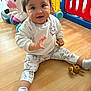 baby, child, toy, floor, indoor, play_area, unicorn_toy, colorful, socks, pants, sweatshirt, smiling, waving, cute, person, wooden_floor, plastic_toys, playpen, happy, young_child