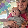 baby, child, woman, balloons, tongue_out, indoor, window, smile, holding, casual_clothing, person, portrait, happy, light, hair, hand, table, celebration, cute, fun