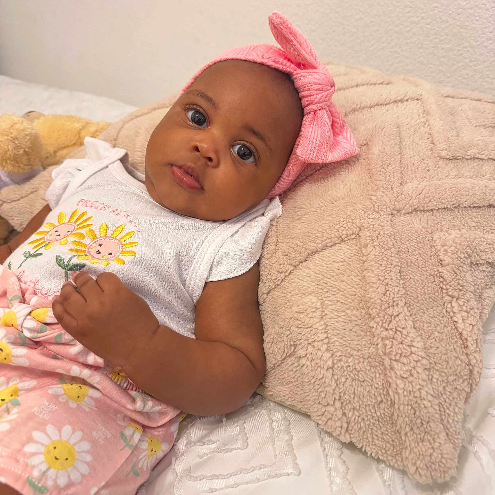 Khanyi joined the competition — help win amazing prizes! baby, child, infant, pink_headband, bow, white_outfit, sunflower_pattern, pillow, blanket, bed, cute, face, skin, eyes, hand, lying_down, indoors, soft_texture, comfortable, adorable