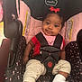 Jamaya is registered to the contest to win money with this photo: baby, child, car_seat, red_bow, pink, black, red_shirt, beige_pants, cast, foot_cast, smile, infant, seat_belt, indoor, cute, young_child, baby_girl, person, sitting, happy