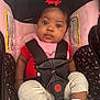 Jamaya is registered to the contest to win money with this photo: baby, child, car_seat, seat_belt, red_bow, pink, black, white_socks, polka_dot, infant, cute, curious, clothing, safety, portrait, indoor, young_child, close_up, person, secure