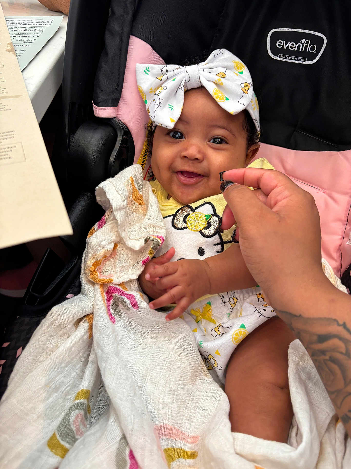 Jamaya is registered to the contest to win money with this photo: baby, child, smiling, headband, bow, blanket, stroller, hand, tattoo, clothing, hello_kitty, pattern, cute, happy, infant, person, indoors, fabric, pink, black