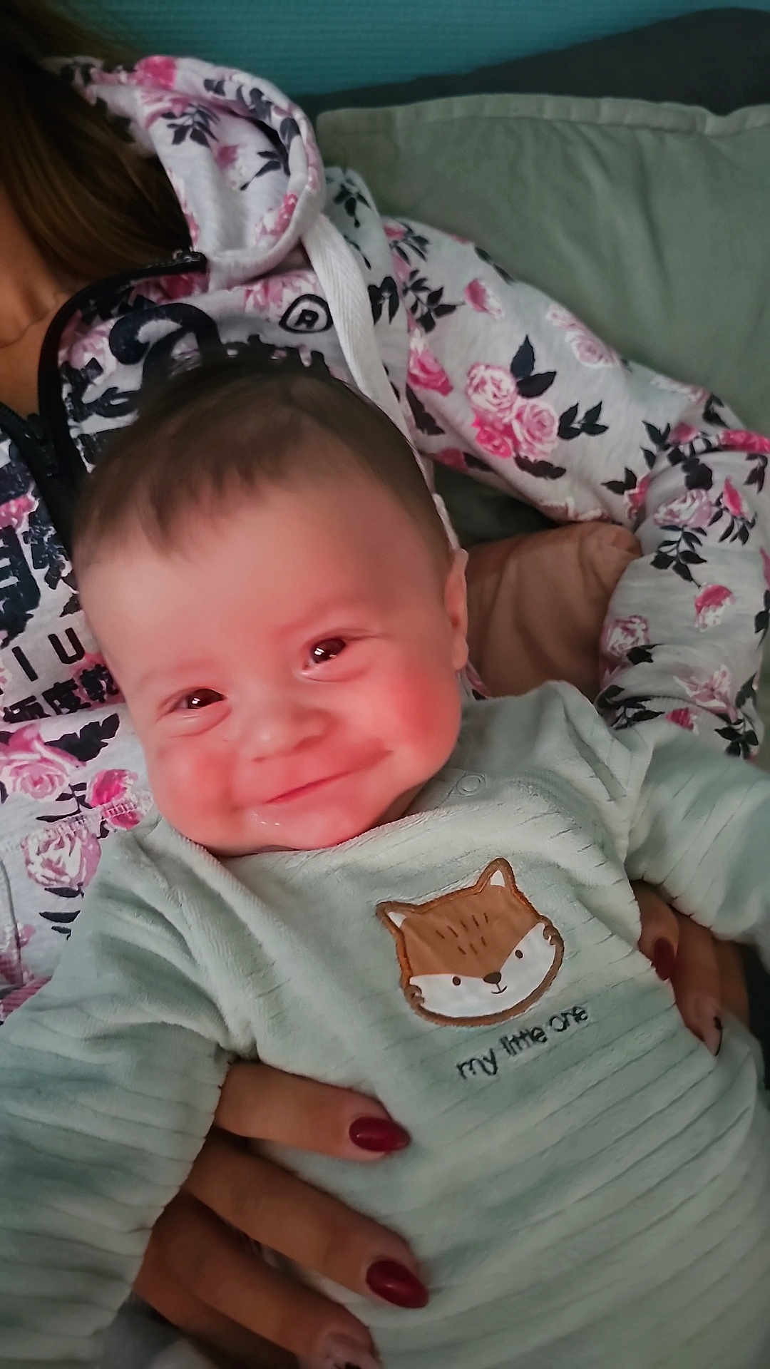 Eliam a rejoint le concours — aidez-le/la à gagner de superbes lots ! baby, smiling, infant, person, hand, clothing, hoodie, floral_pattern, couch, indoor, cute, portrait, child, young, holding, face, happy, cozy, casual, cute_outfit