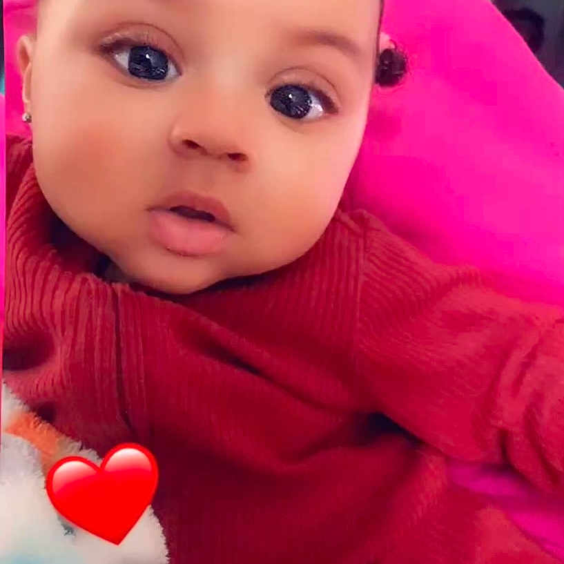 Nakyla Jones joined the competition — help win amazing prizes! adorable, baby, big_eyes, blanket, casual, child, closeup, cozy, expression, face, heart_emoji, indoor, person, pigtails, pink_cushion, portrait, red_outfit, seated, soft_lighting, young_child