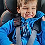 child, toddler, car_seat, blue_hoodie, smiling, happy, seatbelt, car_interior, casual_clothing, young_child, safety_harness, window, daylight, cute, playful, portrait, jeans, seat, boy, hair