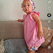 Nayaah participe au concours pour gagner de l'argent avec cette photo : app_interface, button, casual, child, colorful_shorts, couch, curly_hair, expression, furniture, headband, indoor, music_icon, person, phone_screenshot, pink_dress, portrait, rug, standing, toddler, wall