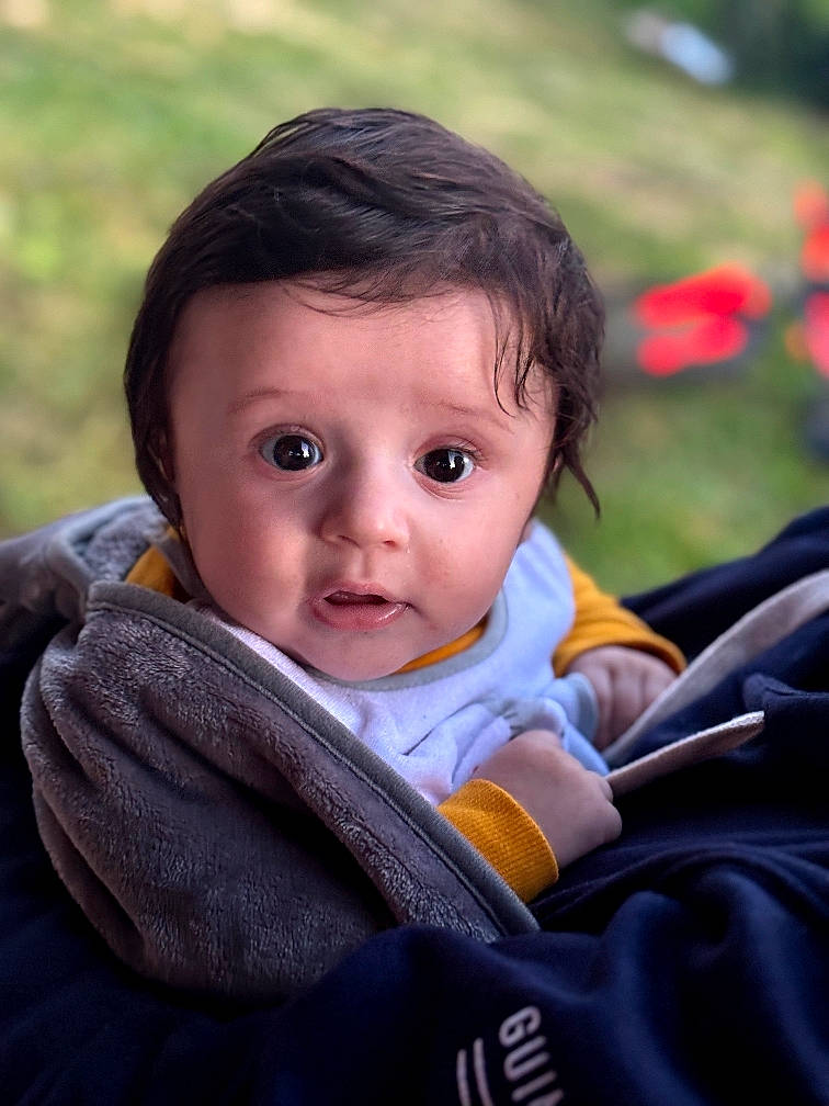 baby, blanket, candid, child, clothing, curious, expression, eyes, face, hair, hand, head, indoors, natural_light, person, portrait, skin, soft_texture, warm, young