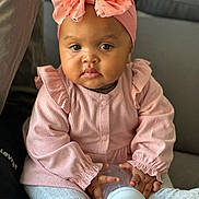 Aina participe au concours pour gagner de l'argent avec cette photo : baby, child, female, pink_clothing, headband, bow, bottle, sitting, couch, indoor, cute, portrait, infant, soft_lighting, hand, sock, curly_hair, person, young_child, casual_clothing