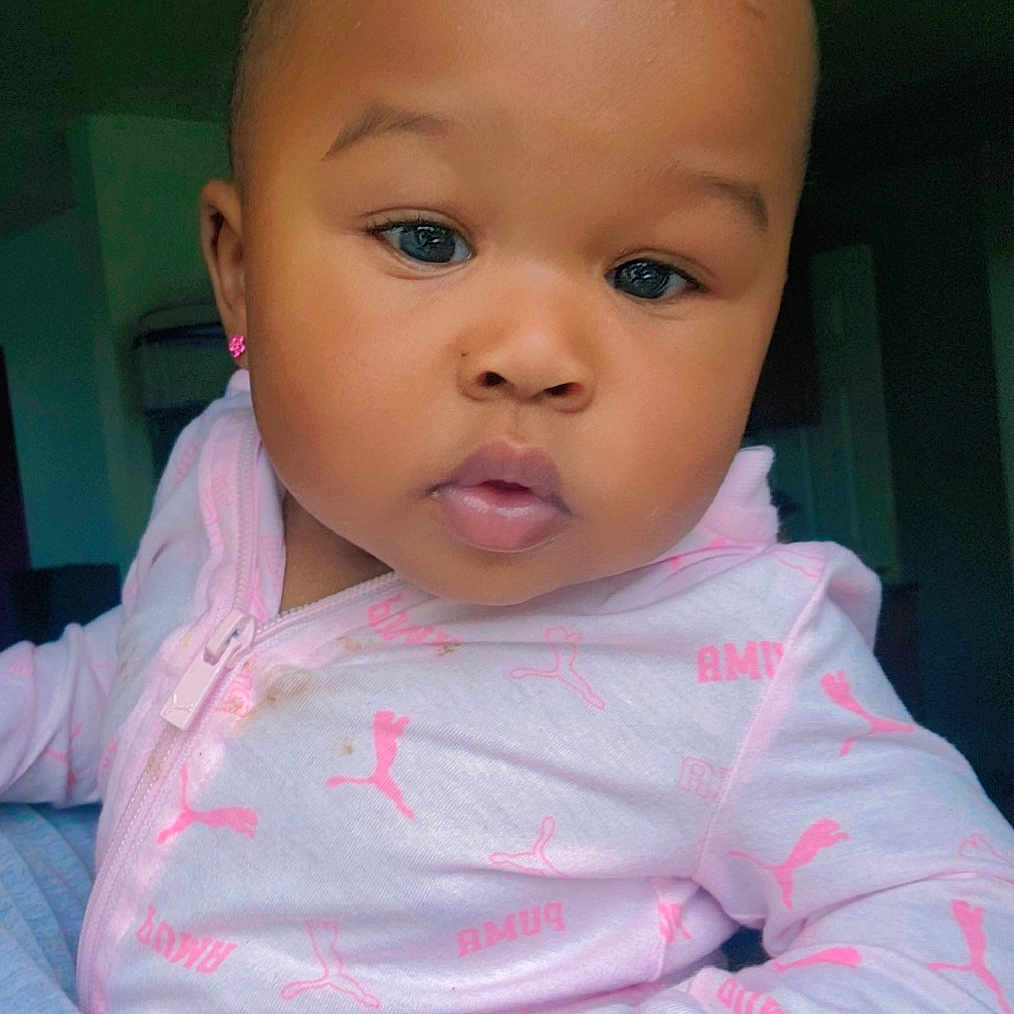 Knowing is registered to the contest to win money with this photo: baby, child, close_up, cozy, cute, earrings, eyes, face, hand, holding, indoor, infant, long_sleeve, person, pink_clothing, portrait, puma_logo, ring, skin, young_child