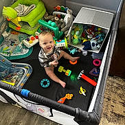 Kane joined the competition — help win amazing prizes! baby, playpen, toys, stuffed_animals, smiling, colorful, indoor, child, floor, clothing, plastic_toys, carpet, fabric, play_area, happy, sitting, person, infant, baby_toy, soft_toys