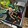 baby, playpen, toys, stuffed_animals, smiling, colorful, indoor, child, floor, clothing, plastic_toys, carpet, fabric, play_area, happy, sitting, person, infant, baby_toy, soft_toys