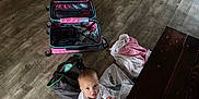 Kane joined the competition — help win amazing prizes! baby, child, floor, wooden_floor, suitcase, bag, plastic_bag, towel, table, baby_gate, container, indoor, person, clothing, sitting, wood, shelves, storage, home, curious