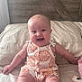 baby, infant, smiling, sitting, romper, orange_pattern, couch, indoor, wooden_wall, cute, child, happy, skin, person, clothing, cute_outfit, fun, portrait, young_child, comfortable