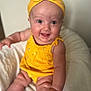 baby, smiling, yellow_clothing, headband, infant, happy, cute, sitting, soft_cushion, indoors, child, portrait, skin, cheeks, face, eyes, hand, legs, bright, colorful