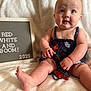 baby, infant, child, sitting, blanket, letter_board, text, clothing, navy_blue, red, white, skin, foot, hand, face, expression, cute, indoors, soft, portrait