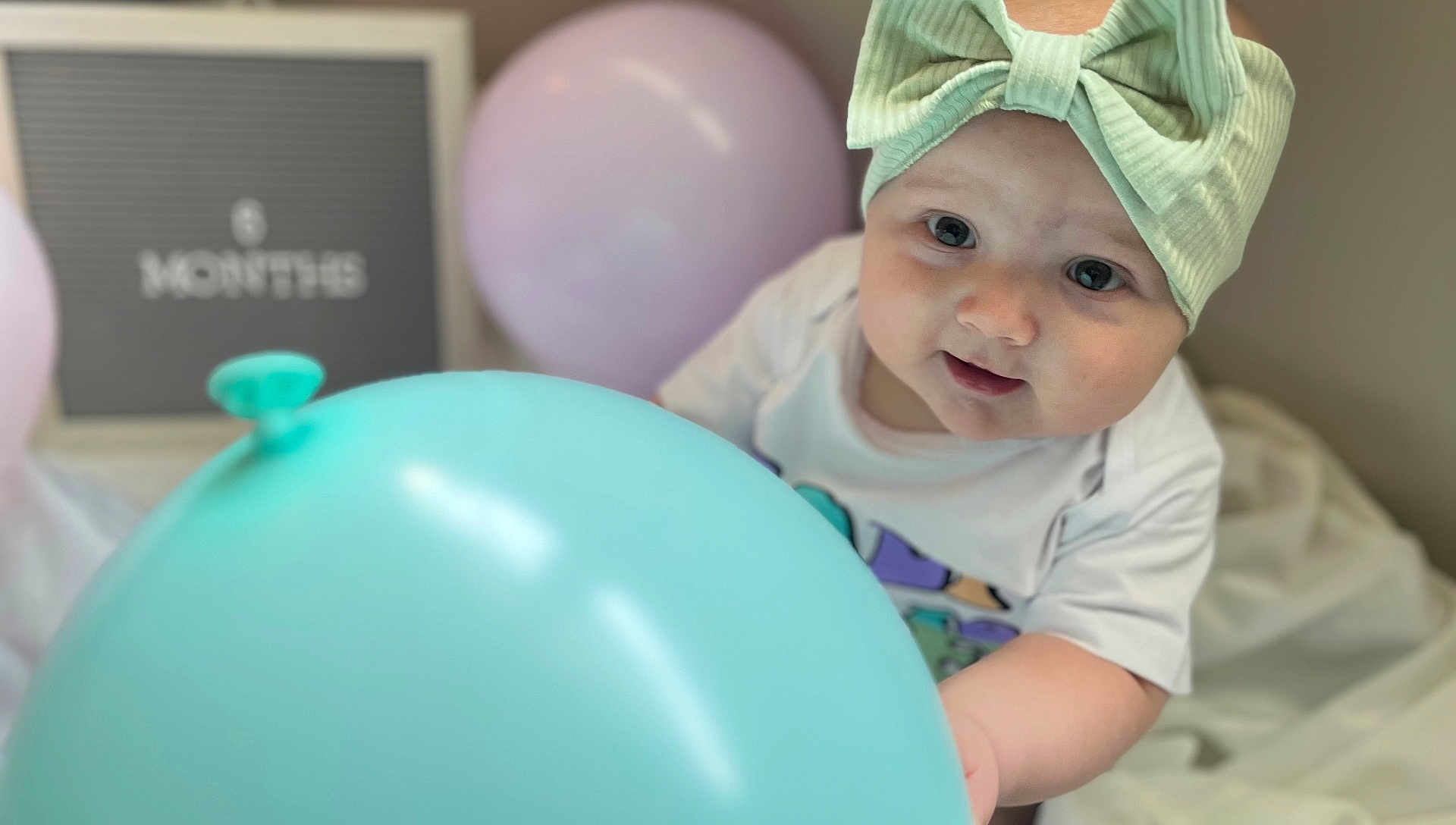Oaklee Mae joined the competition — help win amazing prizes! baby, child, balloon, headband, mint_green, blue_balloon, six_months, sign, pastel_colors, chubby_cheeks, white_clothing, indoor, portrait, cute, smiling, infant, celebration, soft_light, playful, young_child