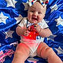 baby, smiling, bow, headband, star, blue, blanket, pattern, clothing, necklace, red_light, happy, infant, cute, sitting, chubby, indoor, portrait, child, celebration