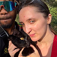 Yuko participe au concours pour gagner de l'argent avec cette photo : black_cat, cat, closeup, dreadlocks, face, glasses, happy, hat, holding, man, nature, outdoor, pet, portrait, selfie, smile, sunlight, trees, woman, yellow_eyes
