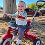 toddler, child, tricycle, outdoor, sunny, happy, smiling, tree, vehicle, grass, play, toy, clothing, vest, pants, socks, handlebars, wheels, daytime, nature