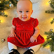 Ka'Lani Grace joined the competition — help win amazing prizes! baby, child, smiling, red_dress, white_tights, black_shoes, christmas, holiday_decorations, pine_branches, ornaments, lights, festive, indoor, portrait, cute, happy, seasonal, celebration, sitting, face