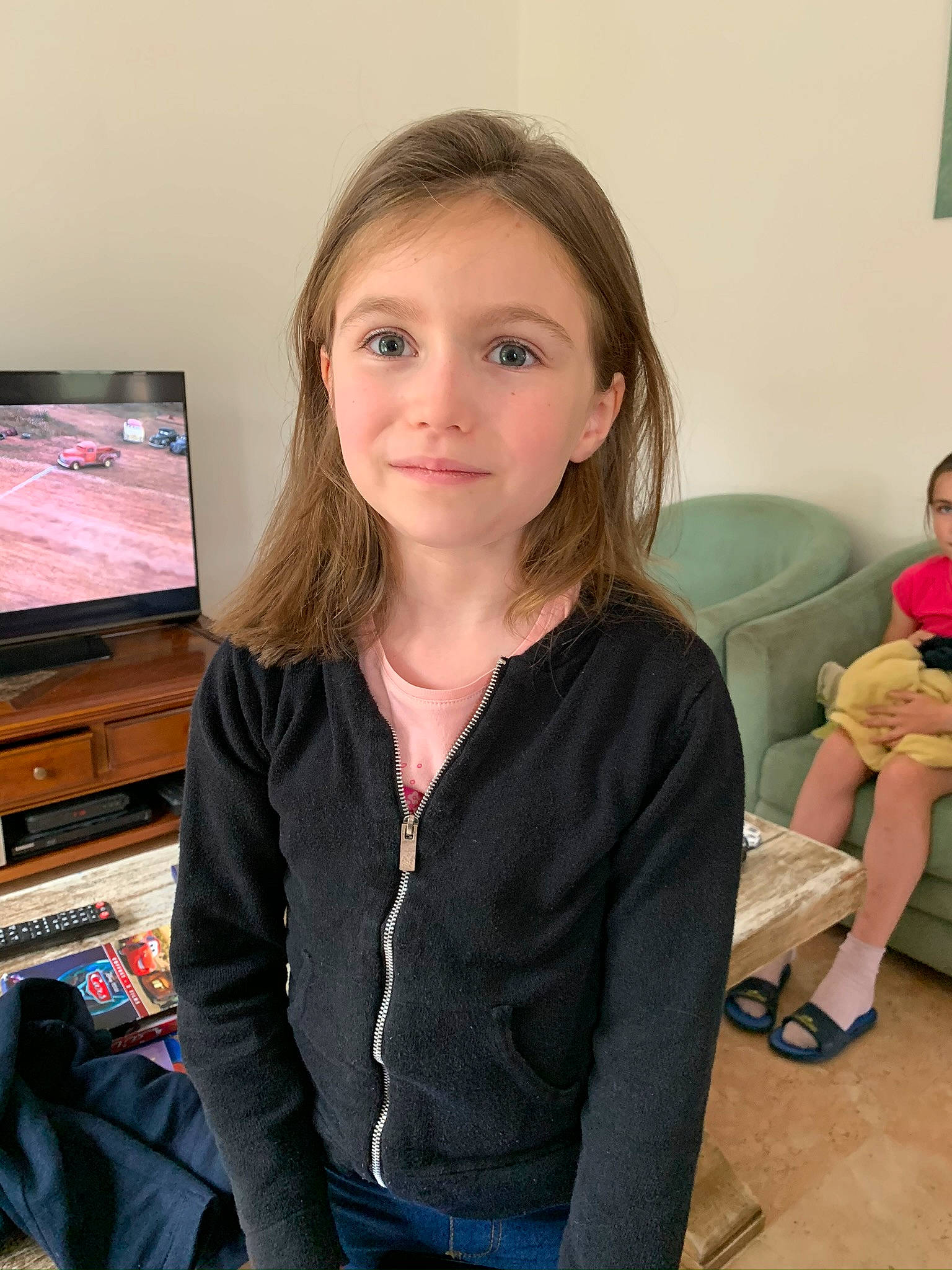 Roxane a rejoint le concours — aidez-le/la à gagner de superbes lots ! brown_hair, child, chin, display_device, event, facial_expression, fun, iris, jewellery, joint, joy, lap, long_hair, person, room, sandal, sitting, sleeve, t_shirt, television