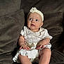 baby, child, infant, white_dress, headband, couch, plush, seated, curious, indoors, soft_lighting, skin, barefoot, portrait, young_child, cute, hands, legs, expression, comfortable
