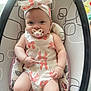 baby, pacifier, headband, infant, child, seat, pattern, white_clothing, orange_bows, cute, indoor, soft_lighting, plush_cushion, baby_girl, portrait, smiling, skin, hand, legs, comfort