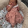 Aaira is registered to the contest to win money with this photo: baby, infant, pink_dress, white_socks, face, hand, cushion, blanket, patterned_blanket, leaf_pattern, soft_texture, newborn, sleeping_area, indoor, cute, small_hands, curious_expression, resting, cozy, child