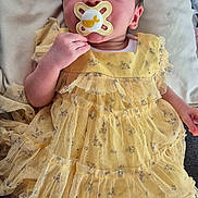 Aaira joined the competition — help win amazing prizes! baby, pacifier, yellow_dress, socks, cushion, soft_fabric, infant, hand, face, clothing, cute, newborn, resting, indoor, person, child, portrait, comfort, skin, small