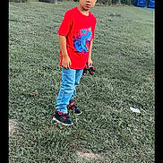 Xadiel Estévez is registered to the contest to win money with this photo: child, boy, grass, park, toy_car, red_tshirt, jeans, sneakers, trees, outdoor, nature, greenery, recycling_bins, casual_clothing, young, standing, playing, daylight, curious, portrait
